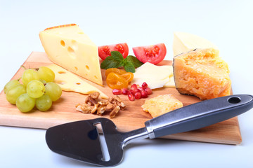 Assortment of cheese with fruits, grapes, nuts and cheese knife on a wooden serving tray.