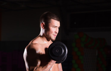 Fototapeta na wymiar Muscular bodybuilder guy doing exercises with dumbbells.
