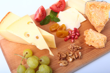 Assortment of cheese with fruits, grapes, nuts and cheese knife on a wooden serving tray.