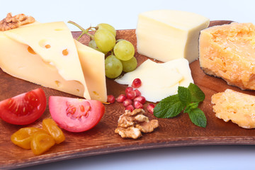 Assortment of cheese with fruits, grapes, nuts and cheese knife on a wooden serving tray.