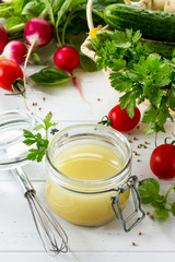 Homemade salad dressing vinaigrette with mustard, olive oil, lemon juice and various fresh vegetables and herbs on a wooden background. The concept of a healthy diet and detox diet.