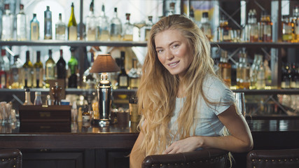 Beautiful blonde woman in evening dress sitting near bar counter and looking at camera