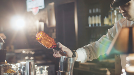 Bartender in hat is preparing cocktail in bar