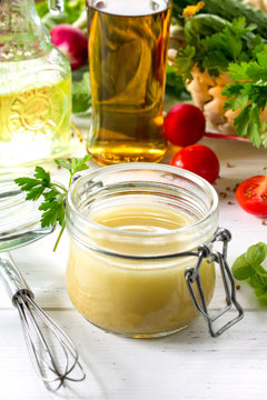 Homemade salad dressing vinaigrette with mustard and olive oil on a white kitchen wooden table.