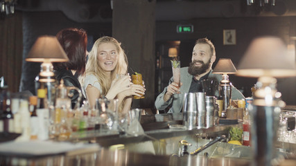 Company of 1 man 2 women are clink glasses in the bar, happy talking and laugh
