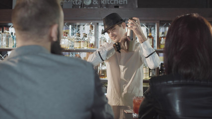 20s bartender is preparing cocktail with shaker behind guests