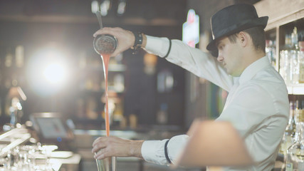 Bartender in hat is preparing cocktail in bar