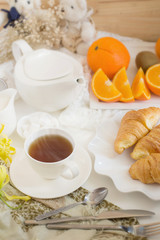 Continental breakfast with gold french croissants fruits and cup of tea on white table in a Morning light. Breakfast concept