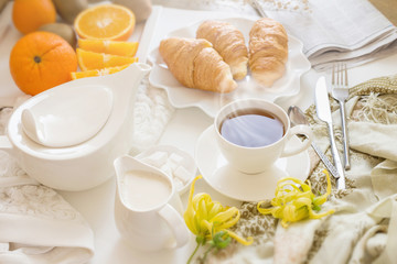 Fototapeta na wymiar Continental breakfast with gold french croissants fruits and cup of tea on white table in a Morning light. Breakfast concept