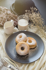 Sugary donut on a black plate and glass of milk on a dark table background. in a windows light. Breakfast concept