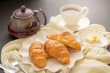 Freshly baked croissants and cup of tea on a white plate on a dark table background. in a windows light. Breakfast concept