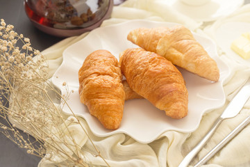 Freshly baked croissants and cup of tea on a white plate on a dark table background. in a windows light. Breakfast concept