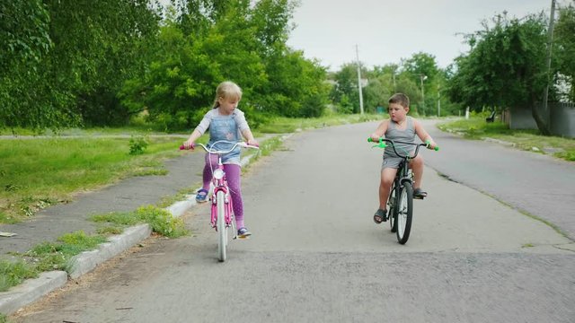 Two carefree children - a girl and a boy ride bicycles on the street. Steadicam shot
