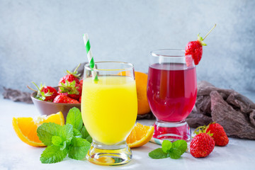 Refreshing summer drinks assortment. Orange juice, strawberry juice, fresh oranges and strawberries on a gray stone or slate background.