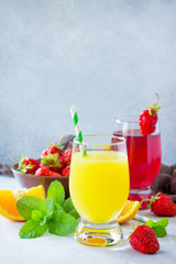 Refreshing summer drinks assortment. Orange juice, strawberry juice, fresh oranges and strawberries on a gray stone or slate background. Copy space.
