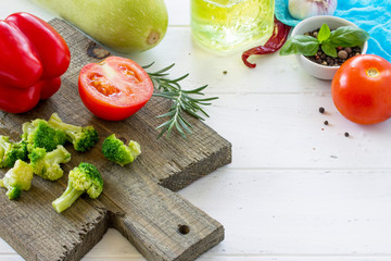 Fresh vegetables - zucchini, tomatoes, sweet pepper, broccoli, olive oil and spices on a wooden cutting board, copy space.