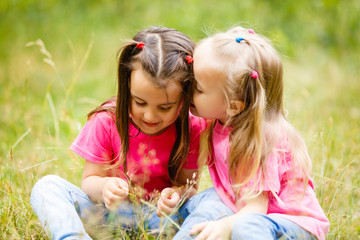 Two little girls are playing and sitting in the park on the grass