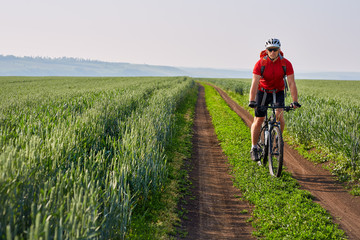 Young cyclist with mountain bicyclist on the path of the field in the countryside against sunrise.