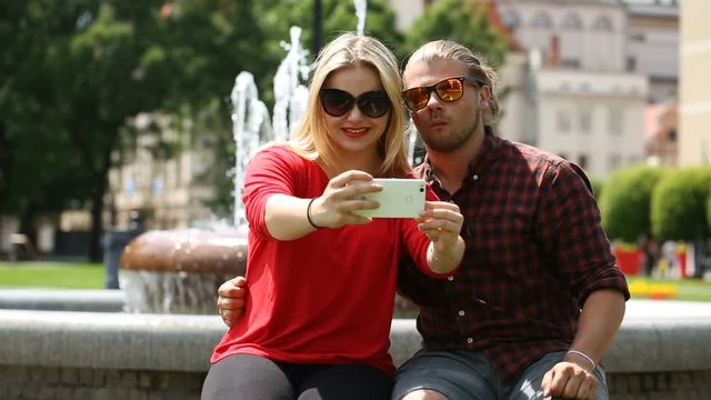 Cute couple sitting next to the fountain and doing photos on smartphone
