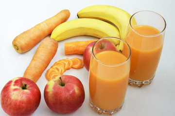 Freshly squeezed juice from carrots, bananas and apples in two glasses near and ingredients