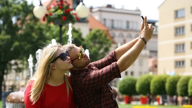 Cute couple having fun while doing photos on smartphone next to the fountain
