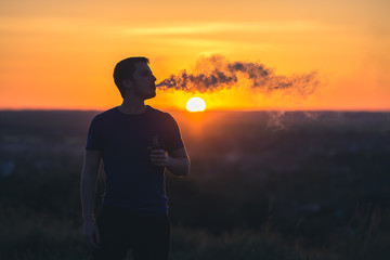 The man smoke an electrical cigarette on the background on the sunrise