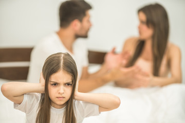 Fototapeta premium The unhappy girl sitting near the arguing parents on the bed