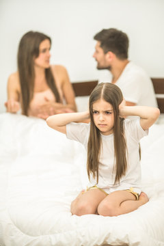The unhappy girl sitting near the arguing parents on the bed