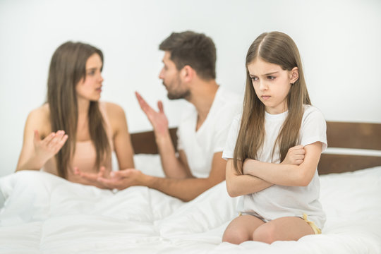 The sad girl sitting near the gesture parents on the bed