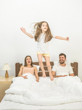 The happy girl jumping on the bed near parents