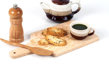 Hot green tea and home made a small sweet cookie with .black sesame, typically round, flat, and crisp.Cookie on .white.