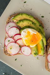Sandwiches with avocado radish cheese and eggs on a rye bread on wooden board on dark background. Healthy breakfast. Vegetarian food.