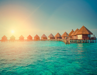 houses over the transparent quiet sea water  on a sunset , toning. Maldives