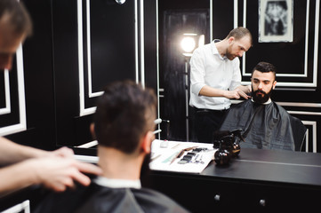 Naklejka na ściany i meble Master cuts hair and beard of men in the barbershop, hairdresser makes hairstyle for a young man