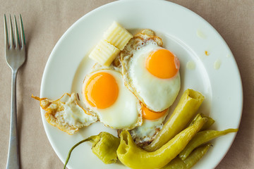 Breakfast. Plate with fried eggs, pieces of cheese and green baked pepper. The dish is on the table, which is covered with a tablecloth. A fork lies next to it. 