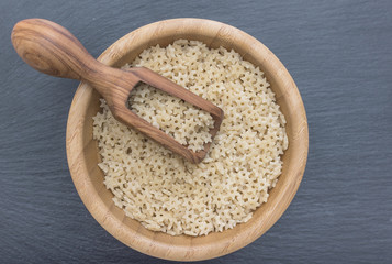Star shaped noodles in a wooden bowl and olive wood scoop on black background of slate or stone