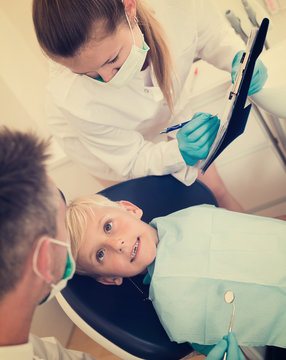 Male dentist with woman assistant are diagnosticating to young patient which is sitting