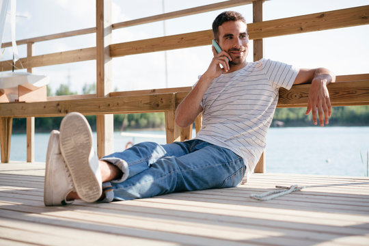 Man relaxing on pier, talking on smartphone