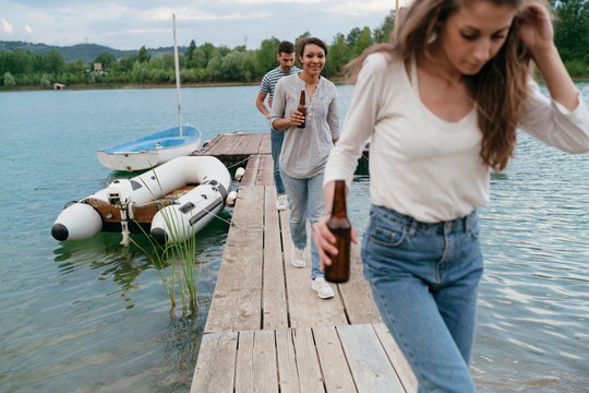 Three friends walking along pier, holding bottled beer