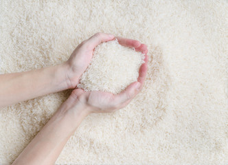 Female hand scooping raw white jasmine rice over texture pattern background, the new soft rice grain grown in Thailand (southeast asian country) good for cooking asian dishes (selective focus)