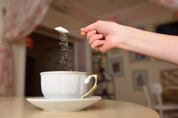 The girl's hand pours sugar into her coffee