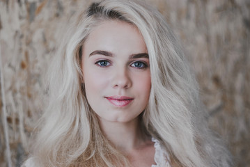 Beautiful stylish blond young woman in a trendy white lace dress near a wooden wall