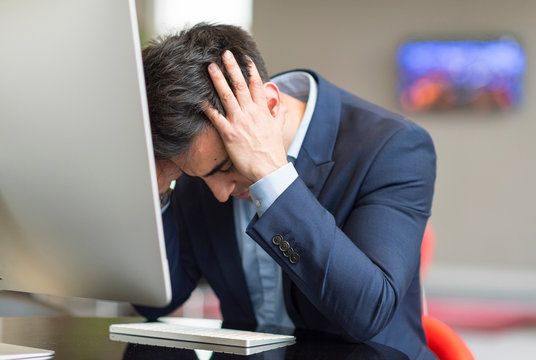 Stressed businessman at office computer with head in hands