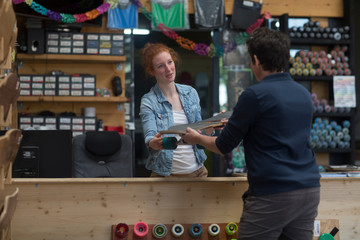 Woman working in skateboard shop, handing skateboard to customer