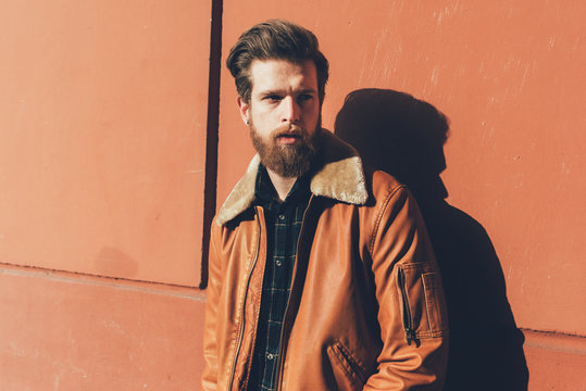 Portrait of cool young bearded man leaning against orange wall