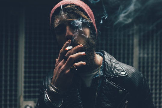Young male hipster smoking cigarette in dark city doorway at night