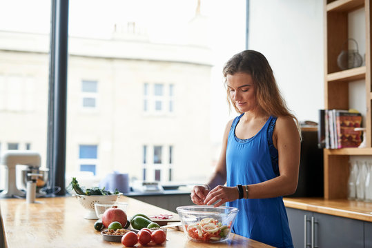 Young woman at kitchen table preparing salad bowl