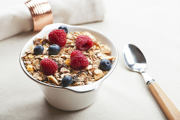 Breakfast cereals with raspberries and blueberries next to spoon.