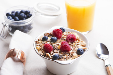 Breakfast cereal with raspberries and blueberries next to orange juice.