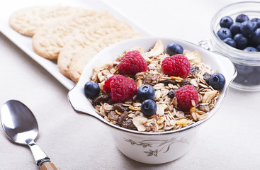 Breakfast cereal with raspberries and blueberries next to plate with cookies.